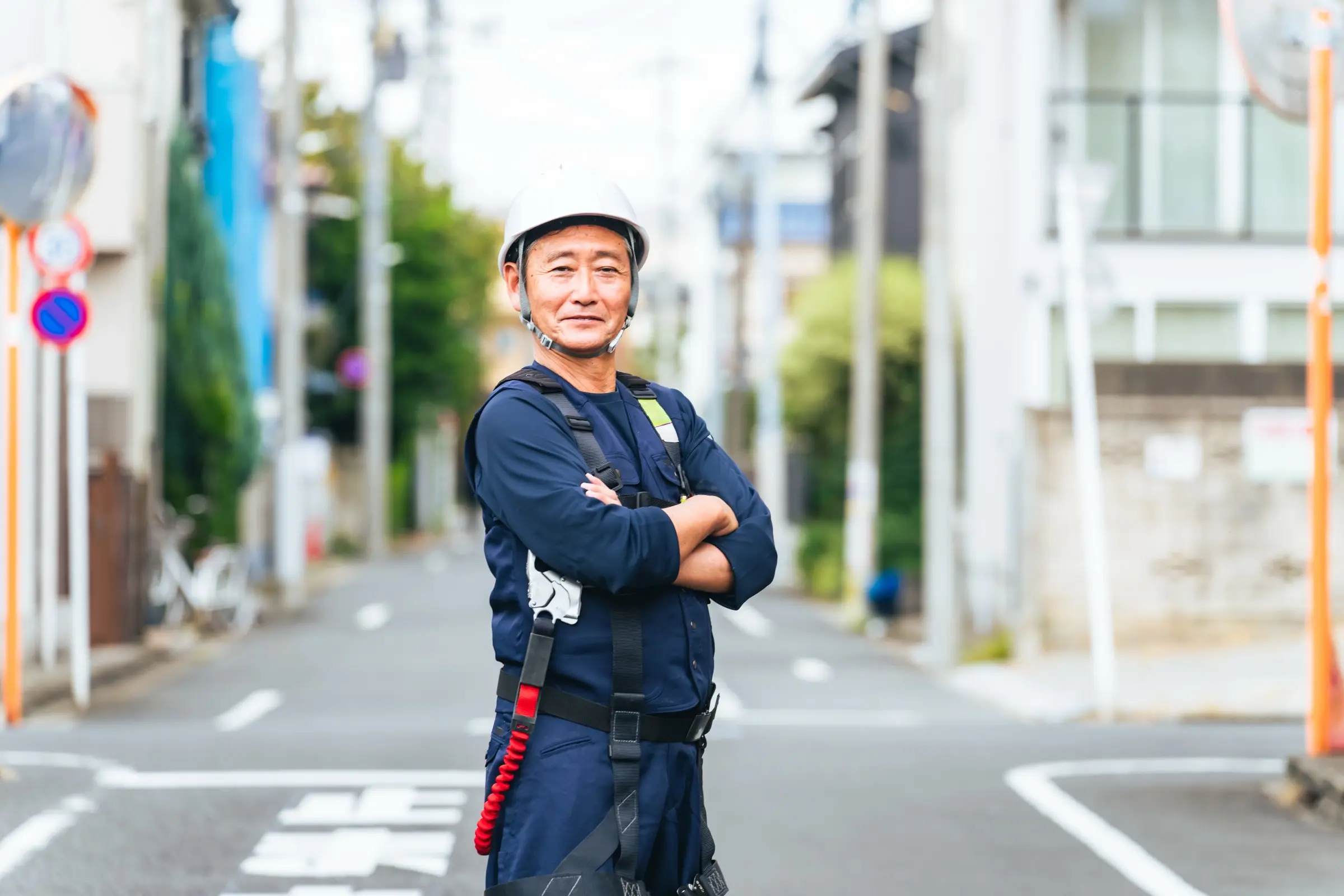 白いヘルメットに作業着姿で腕を組んでほほえむ職人